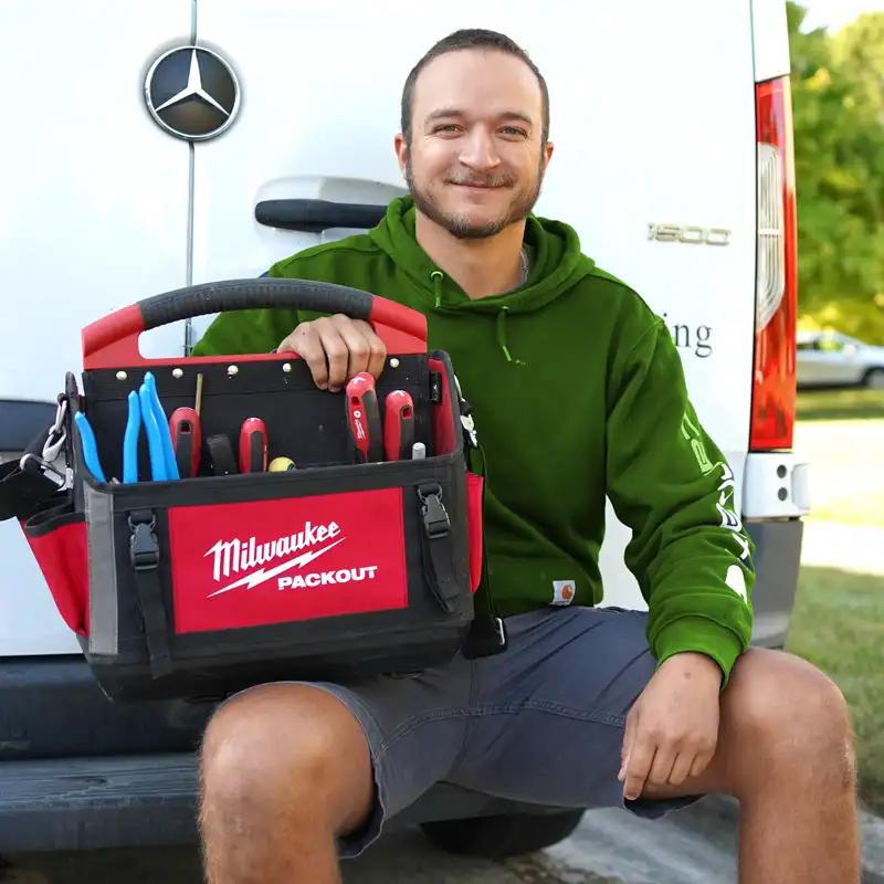 Plumber holding plumbing tools sitting on a five star home services van bumper