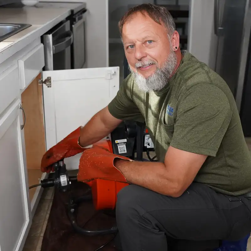 Plumber with equipment kneeling under a sink