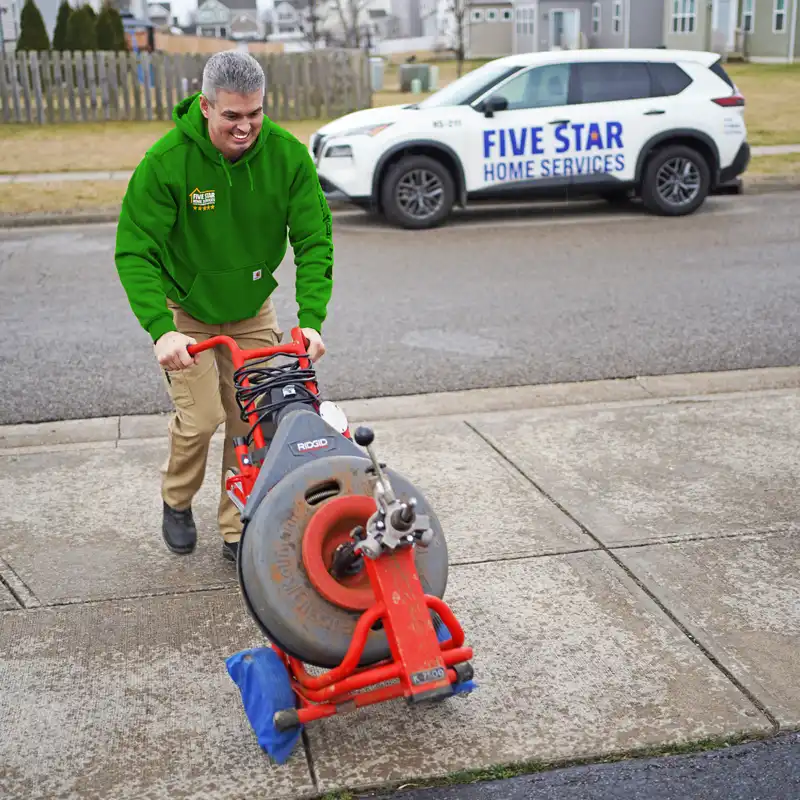 Plumber holding sewer line equipment walking on a driveway